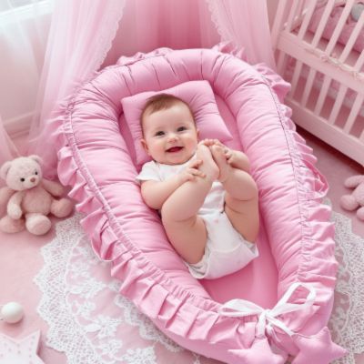 Réducteur de lit portable à volant | Froufrou – Bébé qui sourit dans cocon rassurant rose