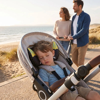 Support de tête et cou bébé | DodoBanana™ vert – enfant qui dort dans poussette au bord de mer
